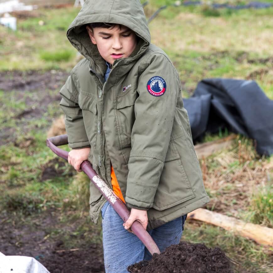 A child wearing a raincoat shovels a pile of soil.