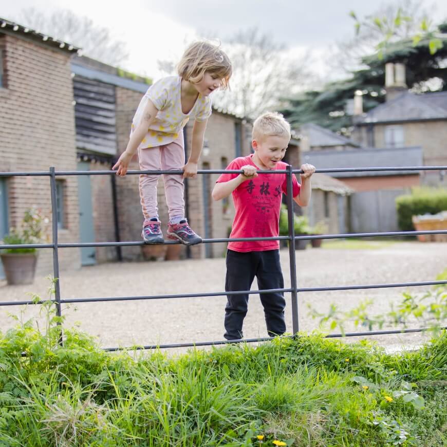 Two children look over a small railing down at some grass on the other side.