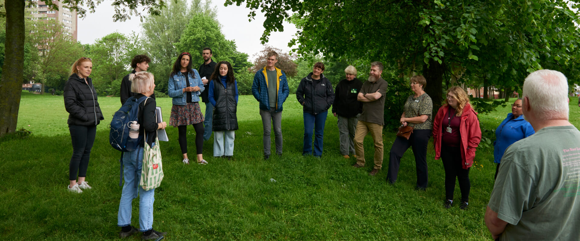 A group of people talking in a park beside trees.