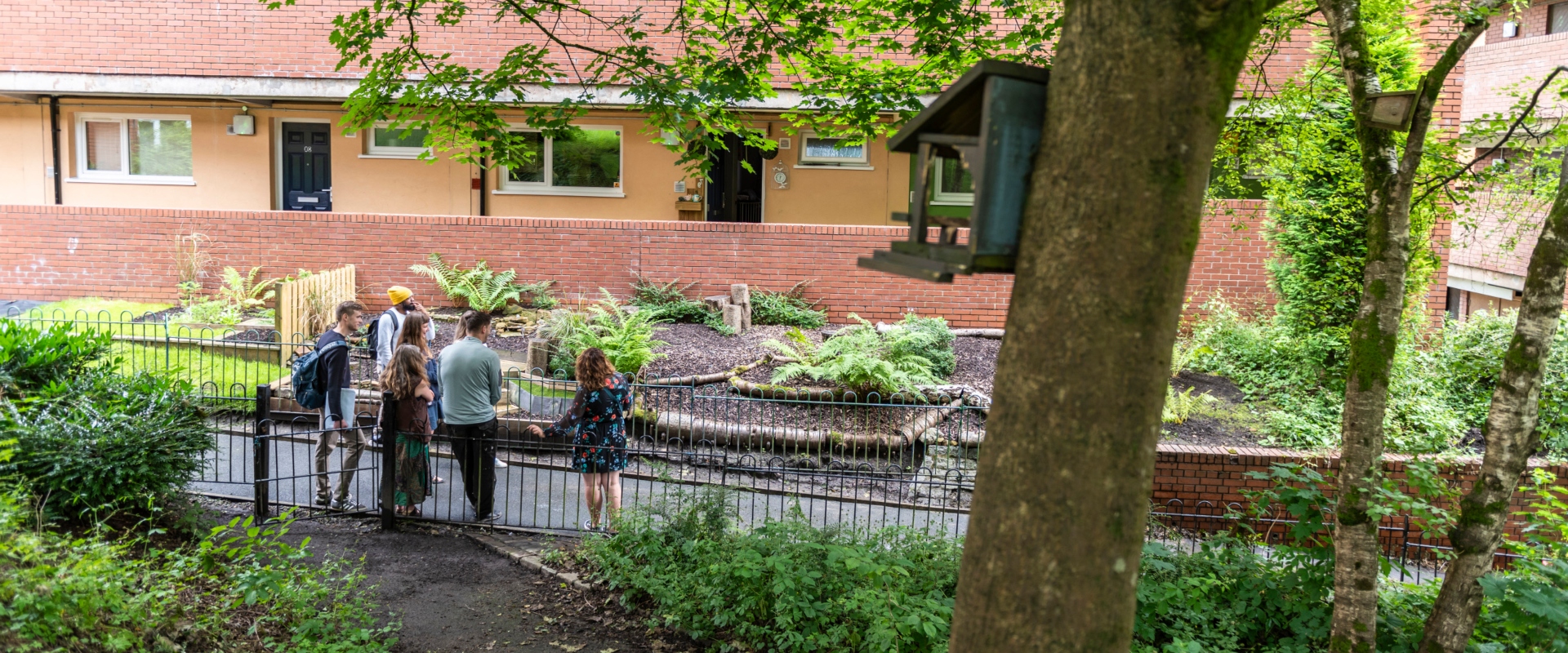 People stood on a path looking at a garden area outside of a flat building.