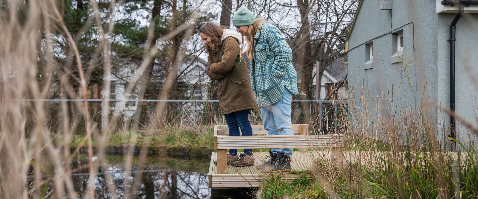 Two people standing on a wooden platform looking over into a wildlife pond.