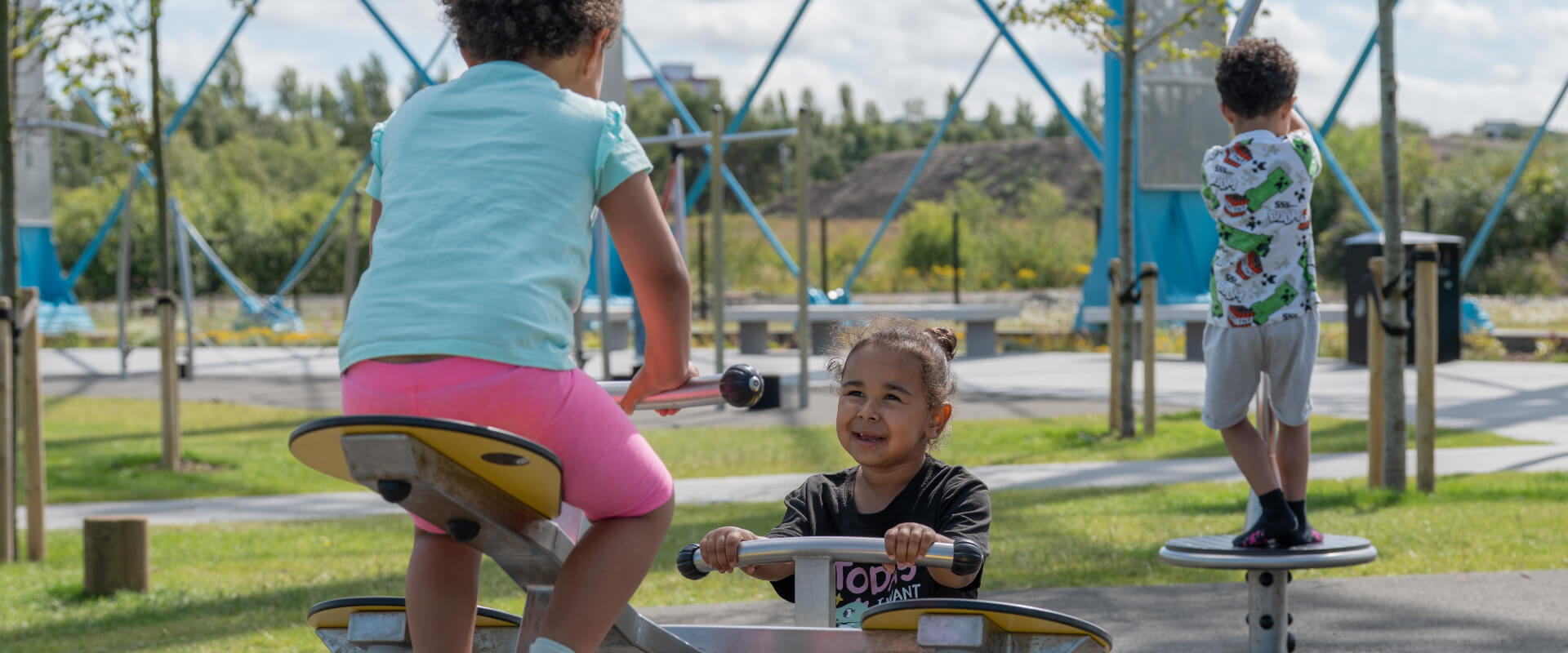 Children smiling and playing on a seesaw in a playground area.