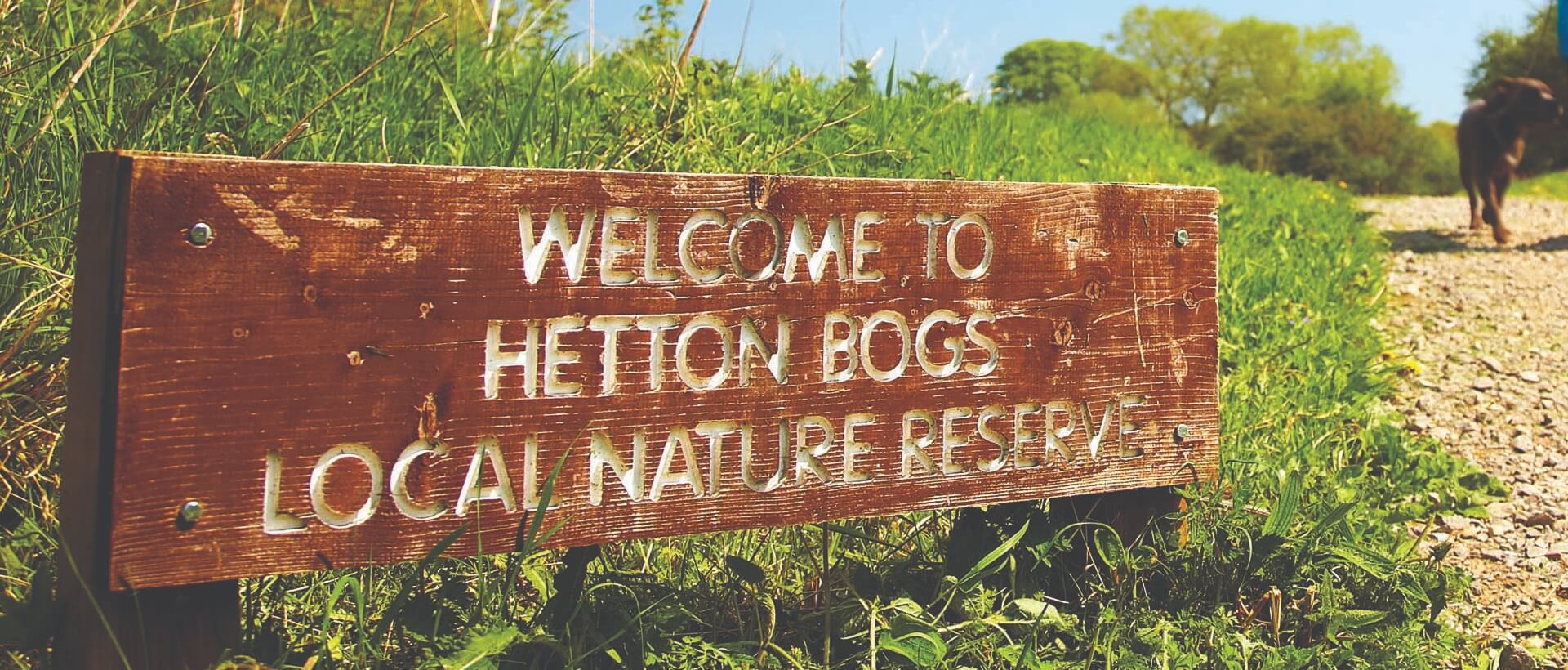 A sign welcoming visitors to Hetton Bogs Local Nature Reserve. There is a dog walking in the corner.