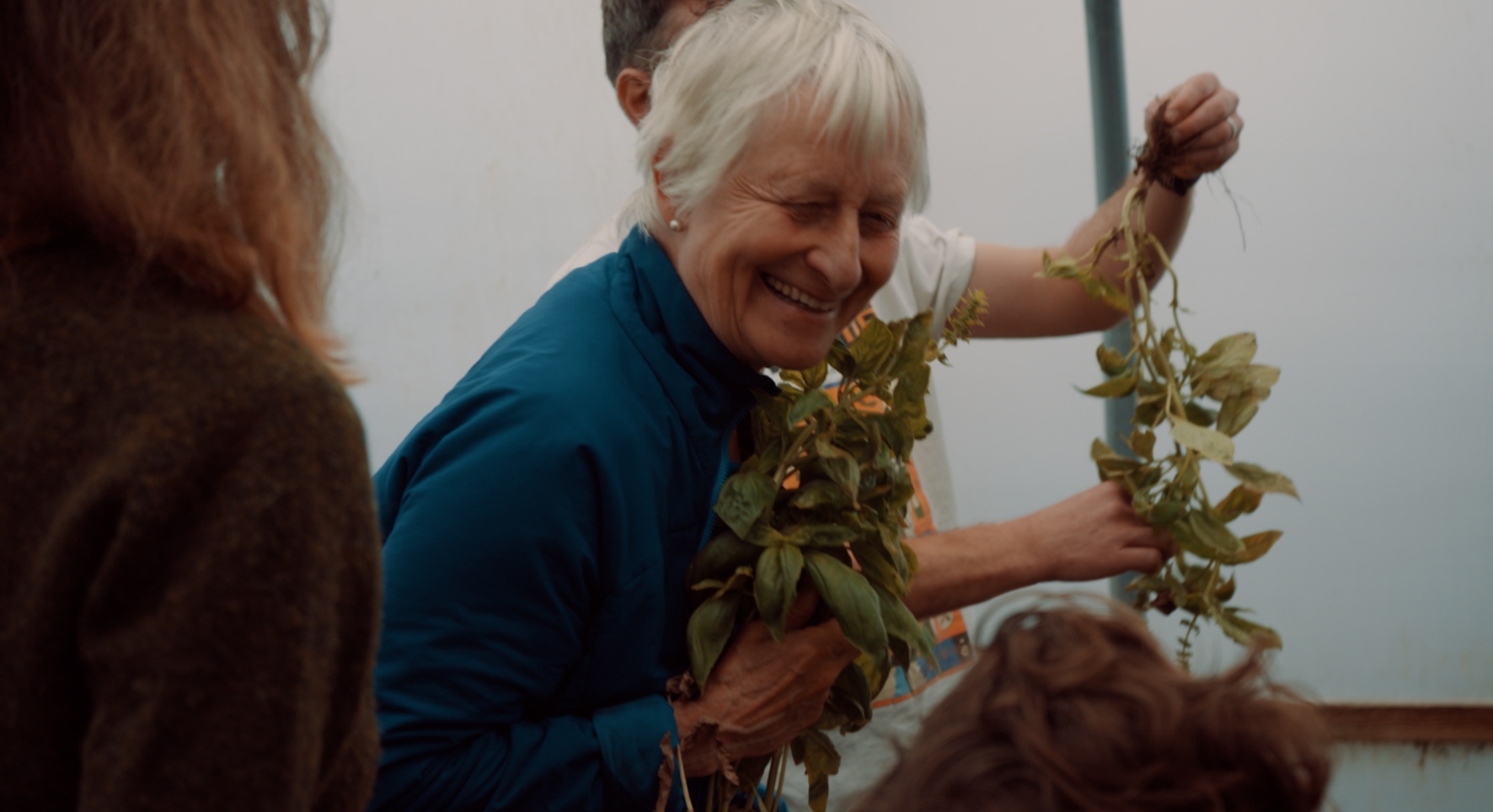 A lady in a blue jacket smiles joyfully as she holds a handful of greenery.