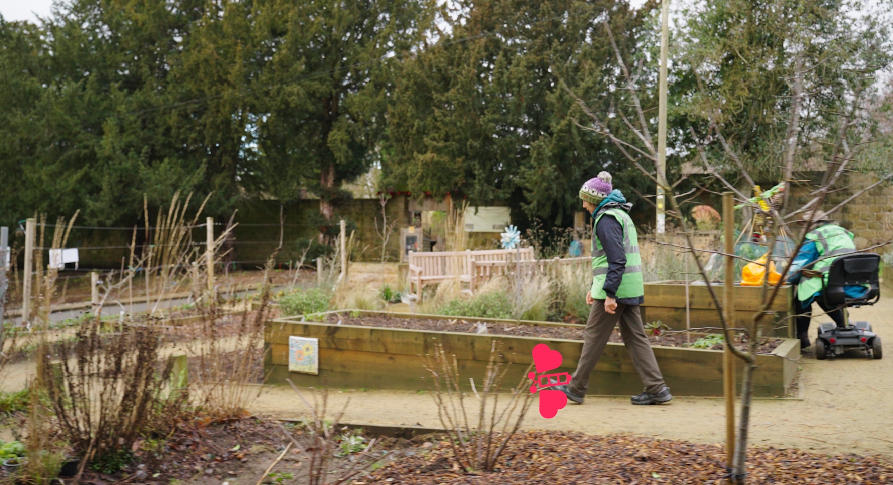 People in green high vis jackets tend to a neat food growing garden on a winters day. There are raised beds with some greenery poking through. A red cartoon moth is superimposed over the image.