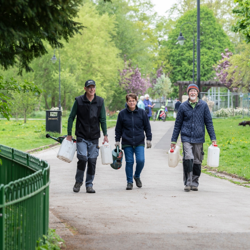 Three people strike through an urban parkland, carrying jerry cans. They look ready to get started with some hands-on tasks.